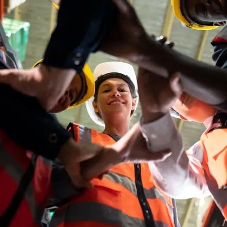 explore-safety-corp A group of construction workers in safety gear, collaborating and joining hands in a circle, exuding teamwork and solidarity.